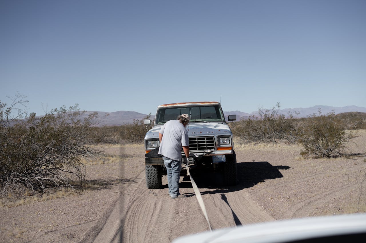 Man assisting stranded pickup truck in arid desert setting.